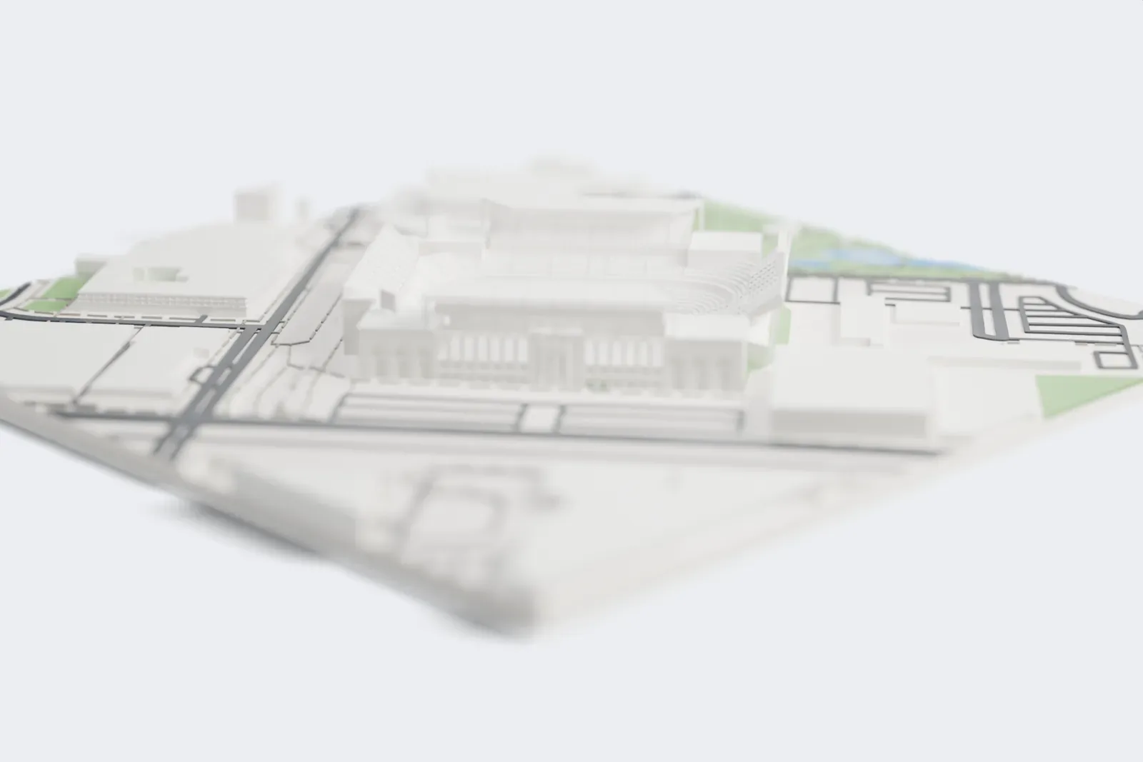 A white 3D print of Kyle Field, a large stadium with stepped seating decks, sloping roof panels and arched, columned side walls, beside a park with ponds and low buildings.