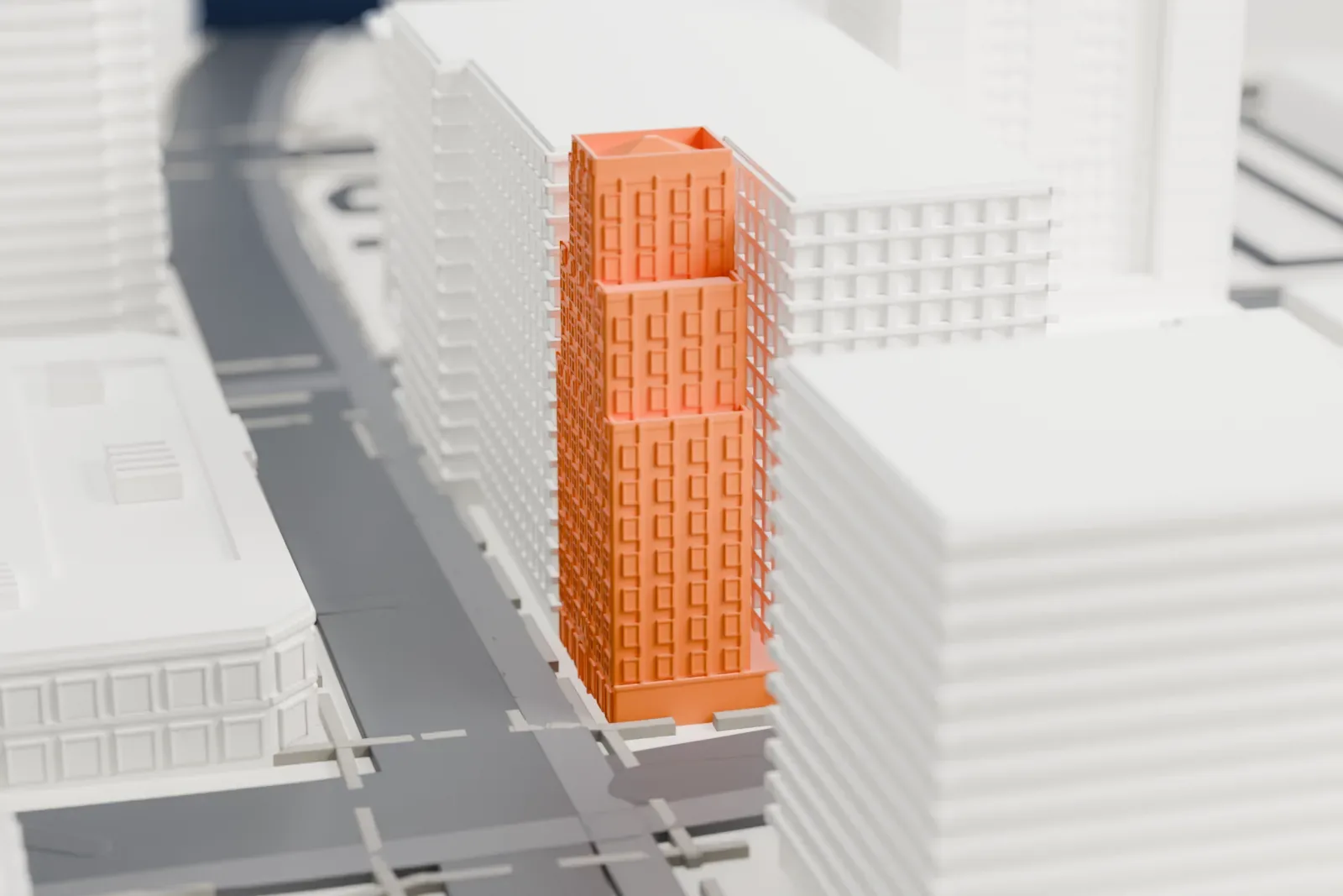 A white 3D print of Luhrs Tower, a narrow stepped tower with a small pyramid roof, standing among larger city buildings beside a wide street.
