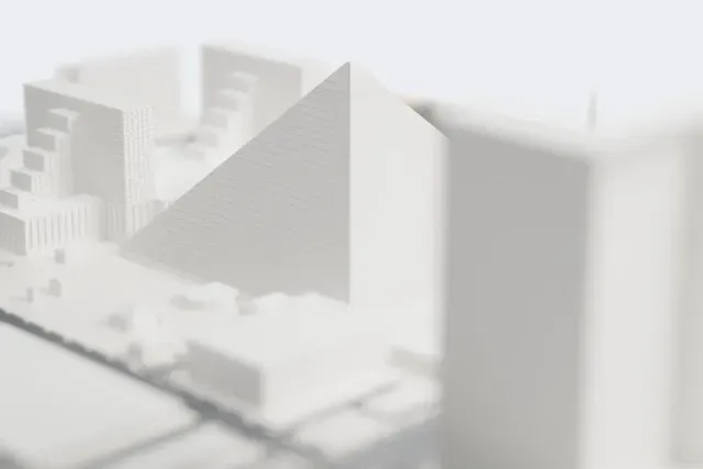 A white 3D print of the Luxor pyramid, a smooth four-sided pyramid with fine horizontal lines on its faces, with stepped hotel towers, roads and low buildings around it.