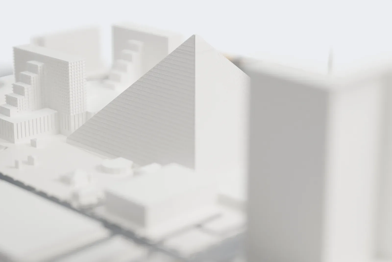 A white 3D print of the Luxor pyramid, a smooth four-sided pyramid with fine horizontal lines on its faces, with stepped hotel towers, roads and low buildings around it.
