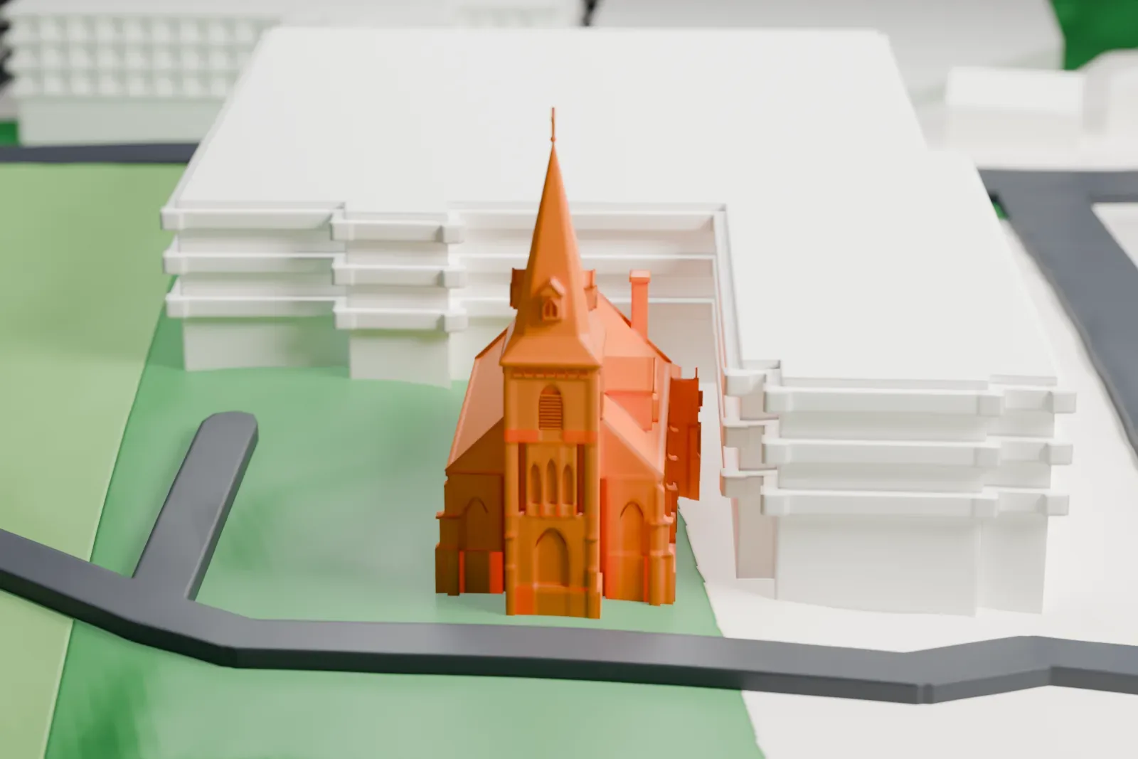 A white 3D print of Madonna Church, a Gothic-style church with a tall spire, on a lawn beside a curving road and large buildings.