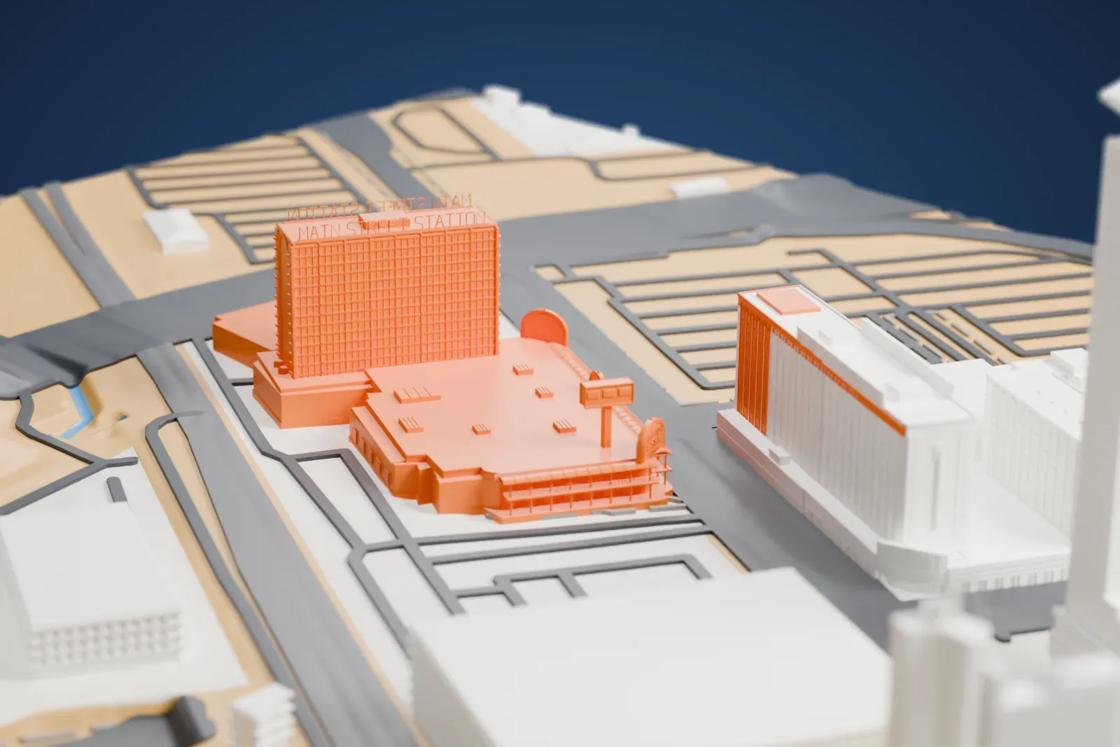 A white 3D print of Main Street Station, a tall hotel slab with rooftop lettering rising above a wide low casino building, among roads and neighboring hotels.