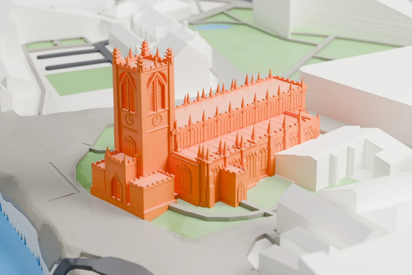 A white 3D print of Manchester Cathedral, a wide church with a tall west tower, among the surrounding streets and buildings of the city center.
