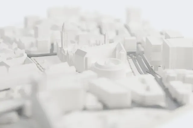 A white 3D print of Manchester Town Hall, a Gothic building with a tall clock tower, corner spires and chimney-lined roofs, beside an open square and surrounded by city buildings.