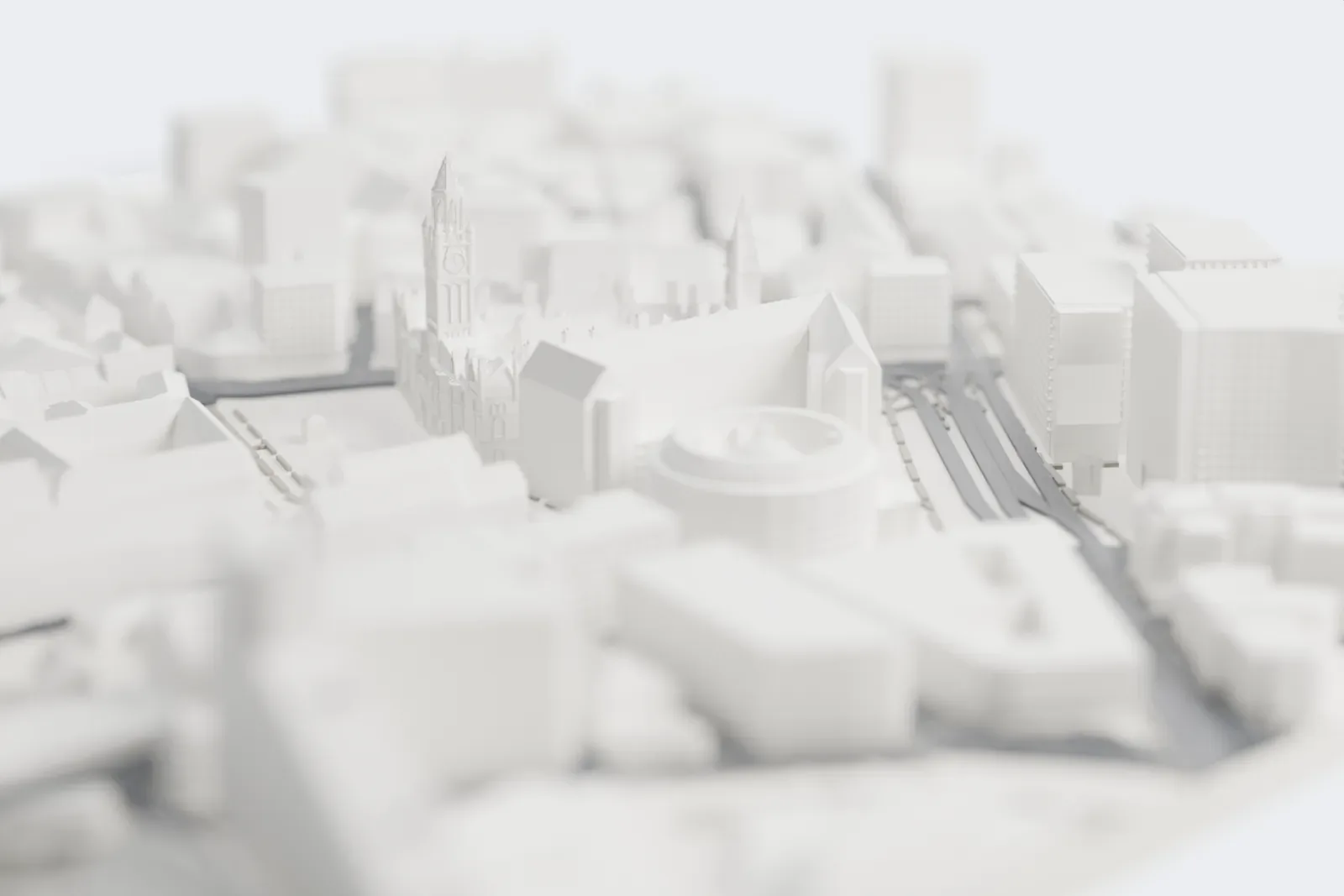 A white 3D print of Manchester Town Hall, a Gothic building with a tall clock tower, corner spires and chimney-lined roofs, beside an open square and surrounded by city buildings.