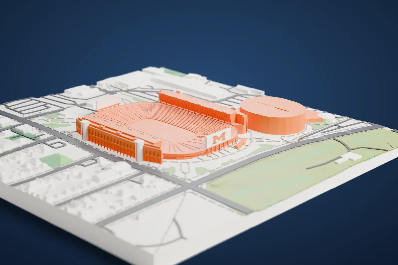 A white 3D print of Michigan Stadium, a large oval bowl with tiered seating and an end-zone scoreboard, surrounded by parking lots, streets and low houses.