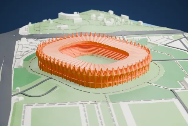 A white 3D print of Milliy Stadium, a ring of pointed cones on columns around a pleated roof over an oval bowl, among the surrounding streets and buildings.