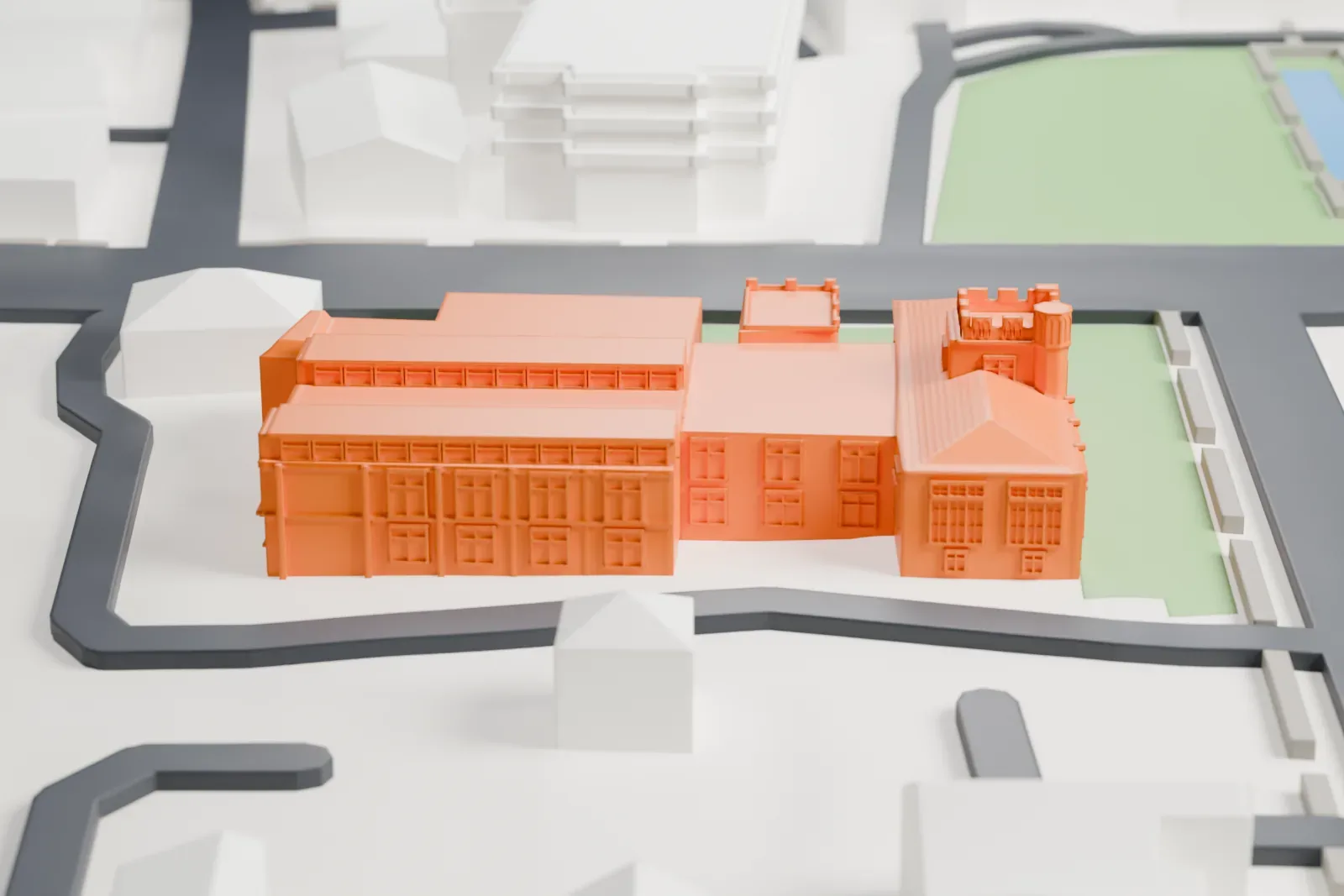 A white 3D print of the Morristown and Morris Township Library, a low building of several connected wings on a green lot, among streets and nearby buildings.