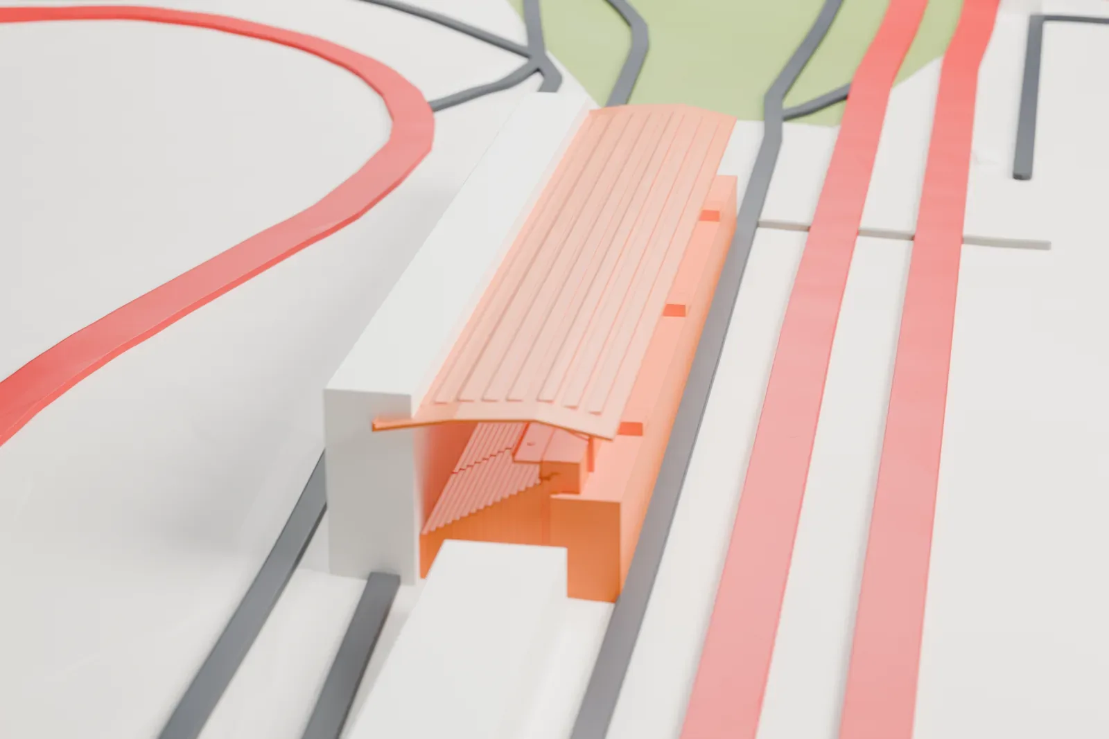 A white 3D print of the Mugello Central Grandstand, a long grandstand with a projecting roof, beside the circuit and surrounding buildings.