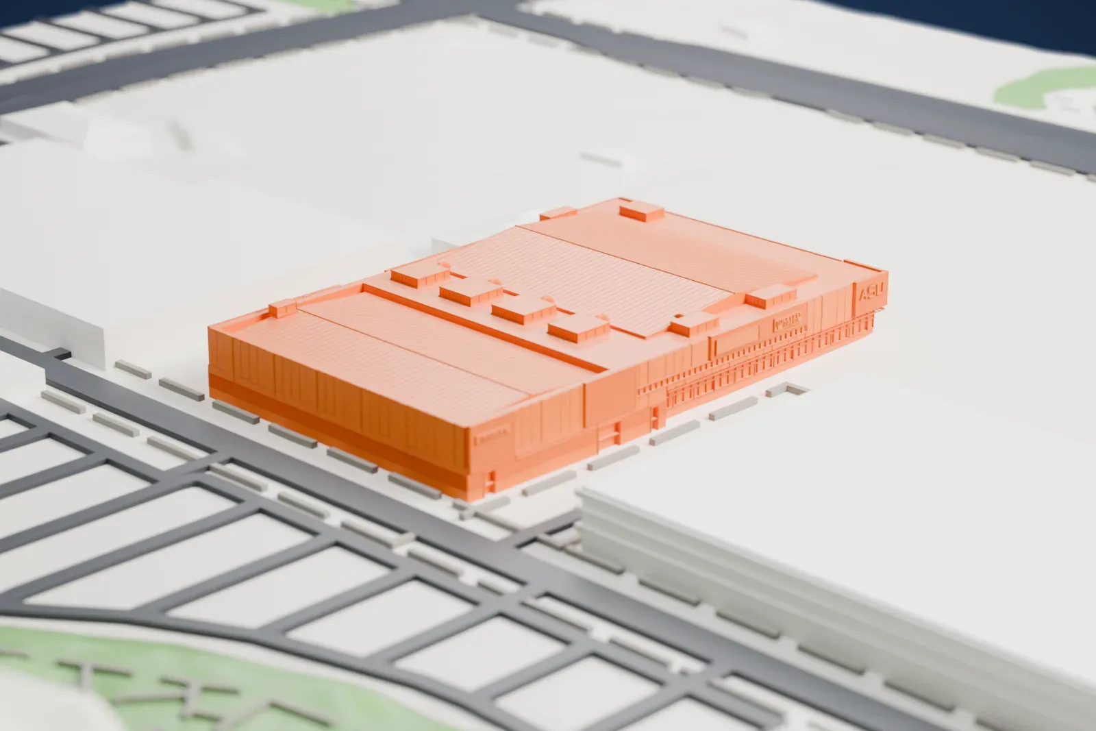 A white 3D print of Mullett Arena, a large rectangular arena with a ridged roof, beside streets, a park corner and small neighboring buildings.