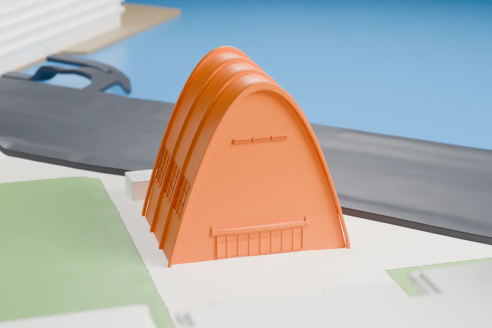 A white 3D print of the Municipal Asphalt Plant, a tall arched building with ribbed sides, beside a road and green lawns, with taller buildings and water beyond.