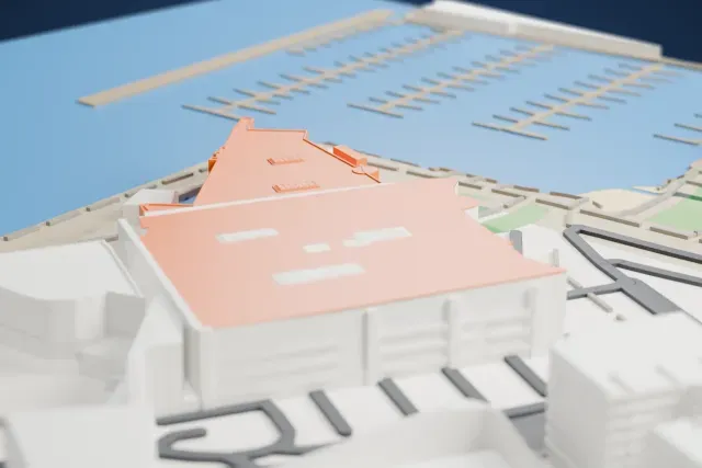 A white 3D print of Te Papa, a wide, low museum building with broad flat roofs and a curved wing, standing beside the water with mid-rise buildings and roads behind it.