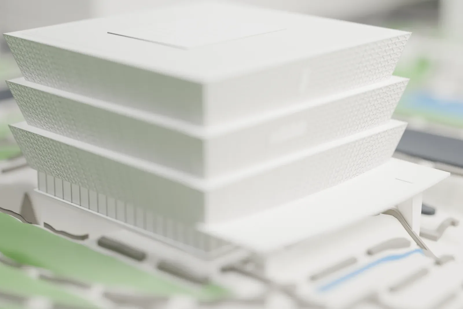 A white 3D print of the National Museum of African American History and Culture, a boxy building of three stacked tiers that widen toward the top, covered in a fine lattice pattern, with paved plazas and green lawns around it.