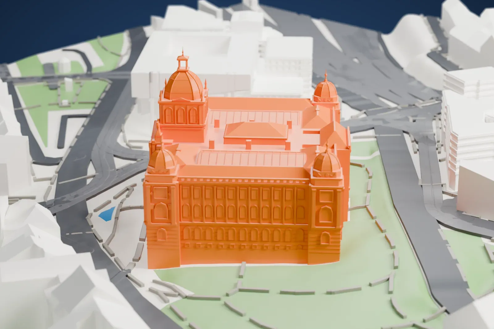 A white 3D print of the National Museum in Prague, a large ornate building with a central dome and smaller corner domes, standing beside green lawns and surrounded by city streets and buildings.