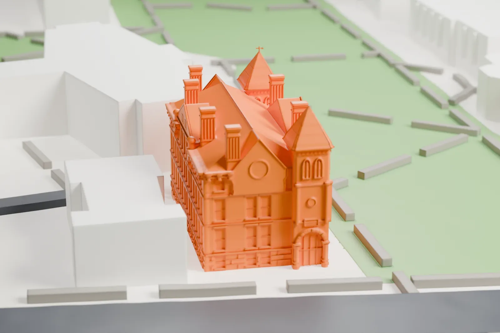 A white 3D print of New Jersey Hall, a large building with pointed turret roofs, tall chimneys and an arched entrance, set on lawns beside paved paths and neighboring buildings.