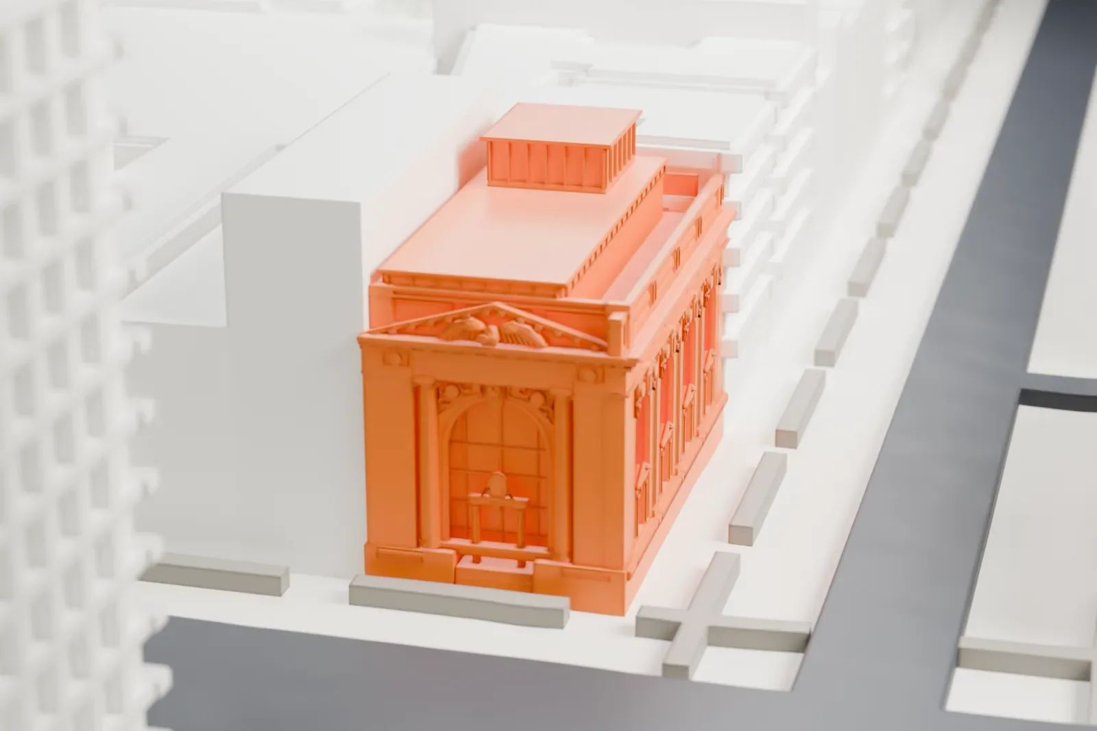 A white 3D print of the New York County National Bank Building, a low building with a columned entrance portico and a detailed cornice, among taller buildings and streets.