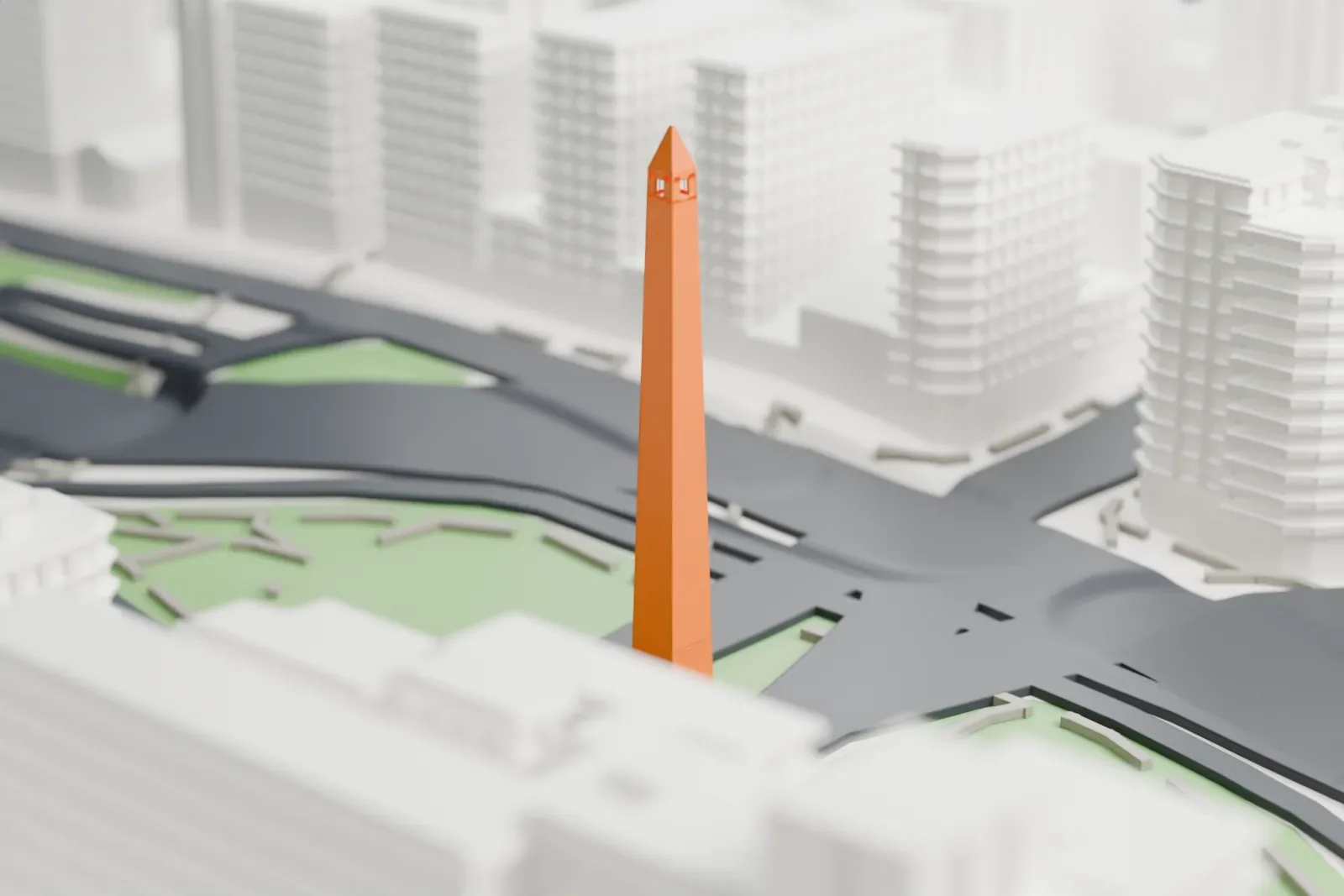 A white 3D print of the Obelisco, a tall slender obelisk with a pointed tip, standing on a green island among wide roads and buildings.