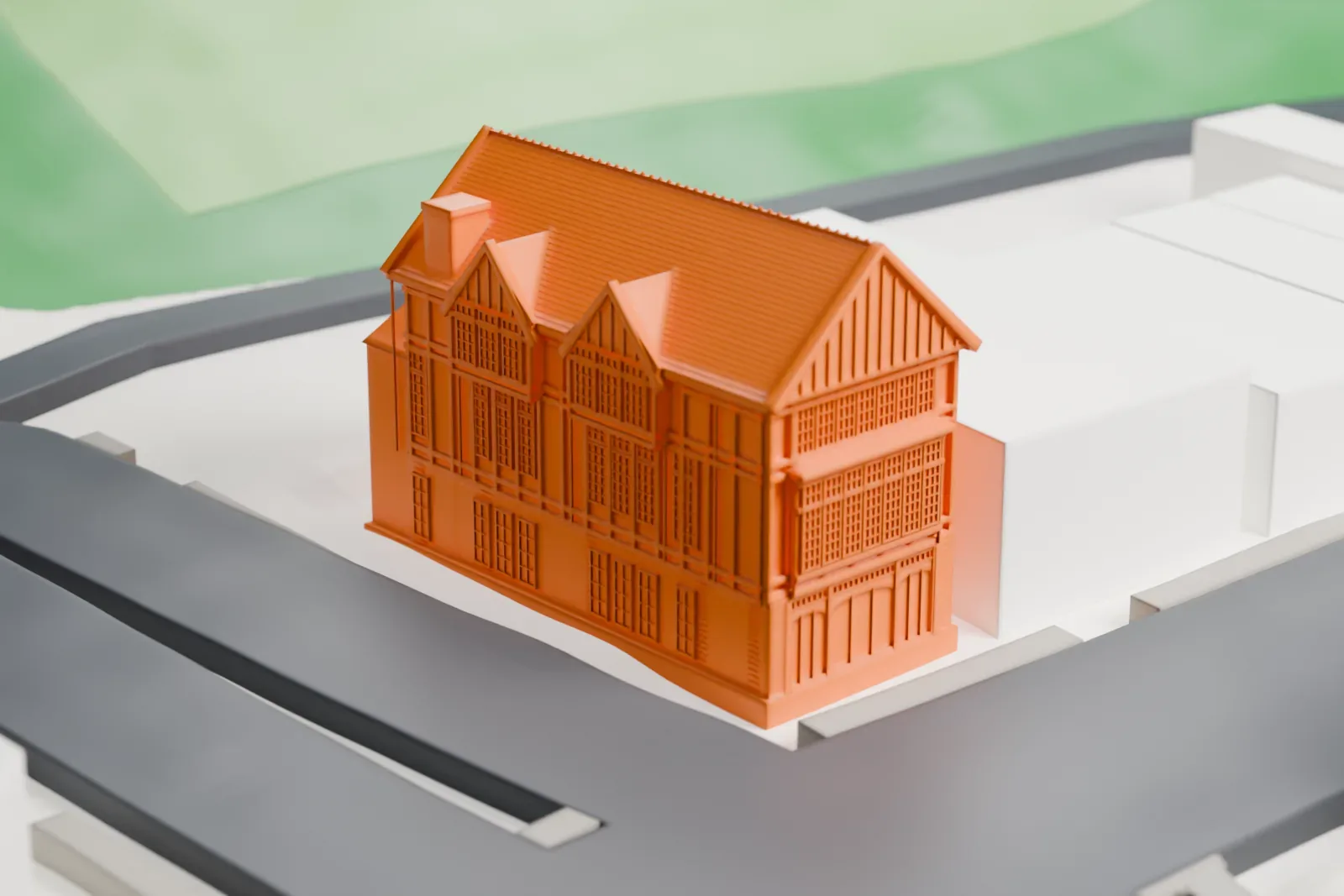 A white 3D print of the Old Glen Cove Post Office, a narrow three-story building with a steep gabled roof, among larger buildings, streets and a patch of lawn.