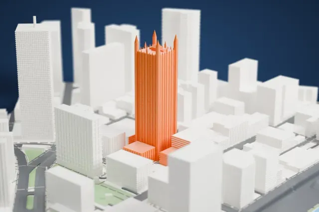 A white 3D print of One PPG Place, a tall square tower with fine vertical ribs and a crown of pointed spires, rising among dense city buildings.