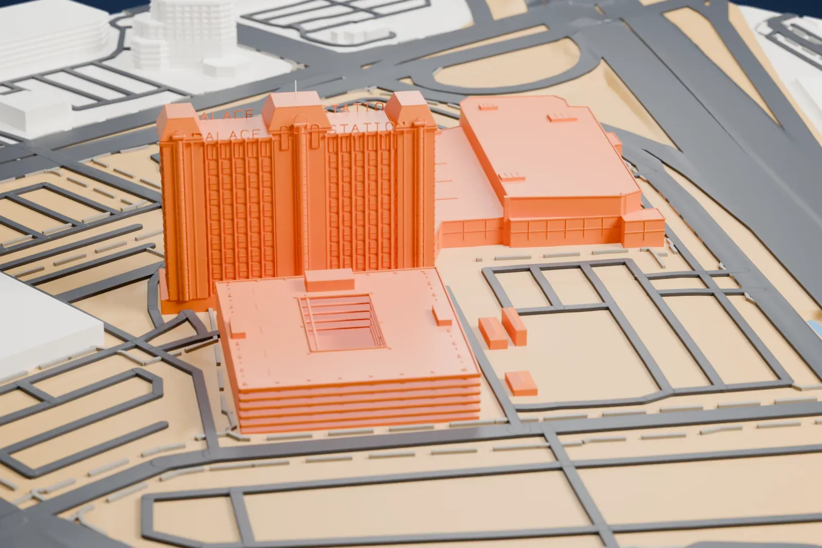 A white 3D print of Palace Station, a tall tower with three wings and pitched caps beside a wide, low building and a square tiered block with an open center, among streets and open lots.
