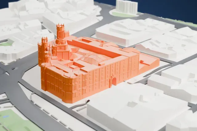 A white 3D print of the Palacio de Cibeles, a large block with a lattice courtyard roof, a central tower and corner turrets, beside wide roads.