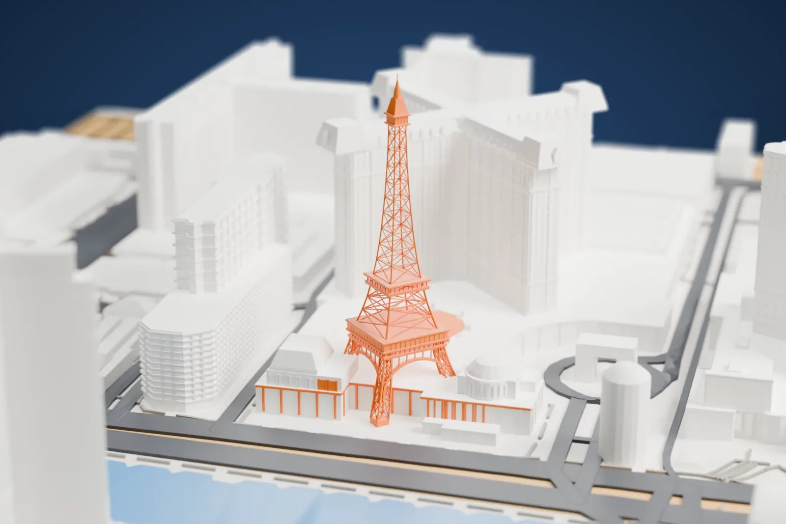 A white 3D print of Paris Las Vegas, an X-shaped hotel tower with a lattice Eiffel Tower replica beside it, surrounded by streets, large buildings and a pool of water.