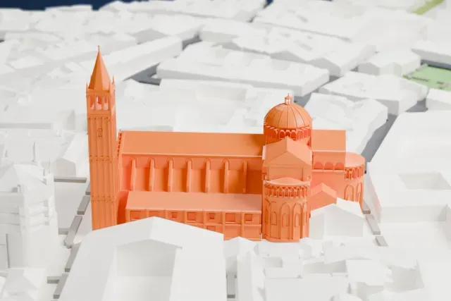 A white 3D print of Parma Cathedral, a long church with a ribbed dome and a tall bell tower with a pointed spire, packed in among nearby buildings.
