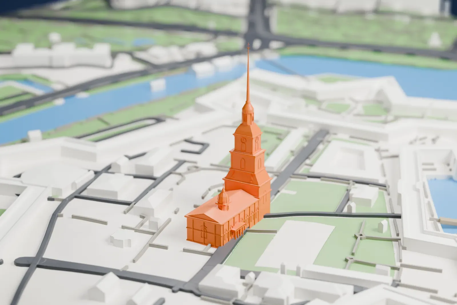 A white 3D print of the Peter and Paul Fortress, a star-shaped fortress with angular walls and a thin central spire, set on an island surrounded by a wide river, with parkland and city districts on the banks.