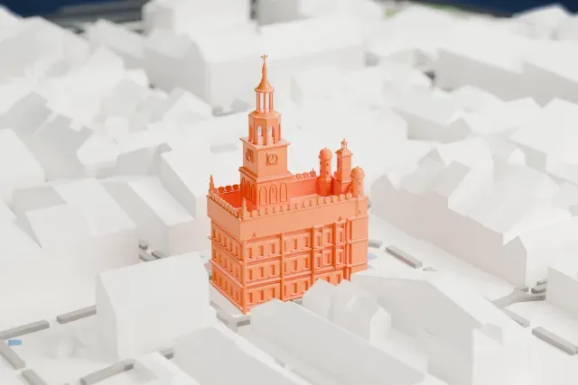 A white 3D print of Poznań Town Hall, a square building with a clock tower topped by an open lantern and spire, arcaded walls and corner turrets, surrounded by closely packed pitched-roof buildings.