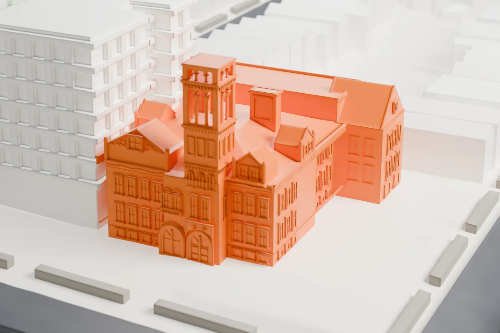 A white 3D print of P.S. 66, a large school building with a tower, standing among rows of small buildings and streets, with a green hillside nearby.