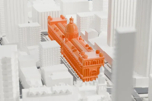 A white 3D print of the Queen Victoria Building, a long low building with a large central dome, smaller domes at its corners and a ribbed barrel roof, surrounded by tall city towers and streets.
