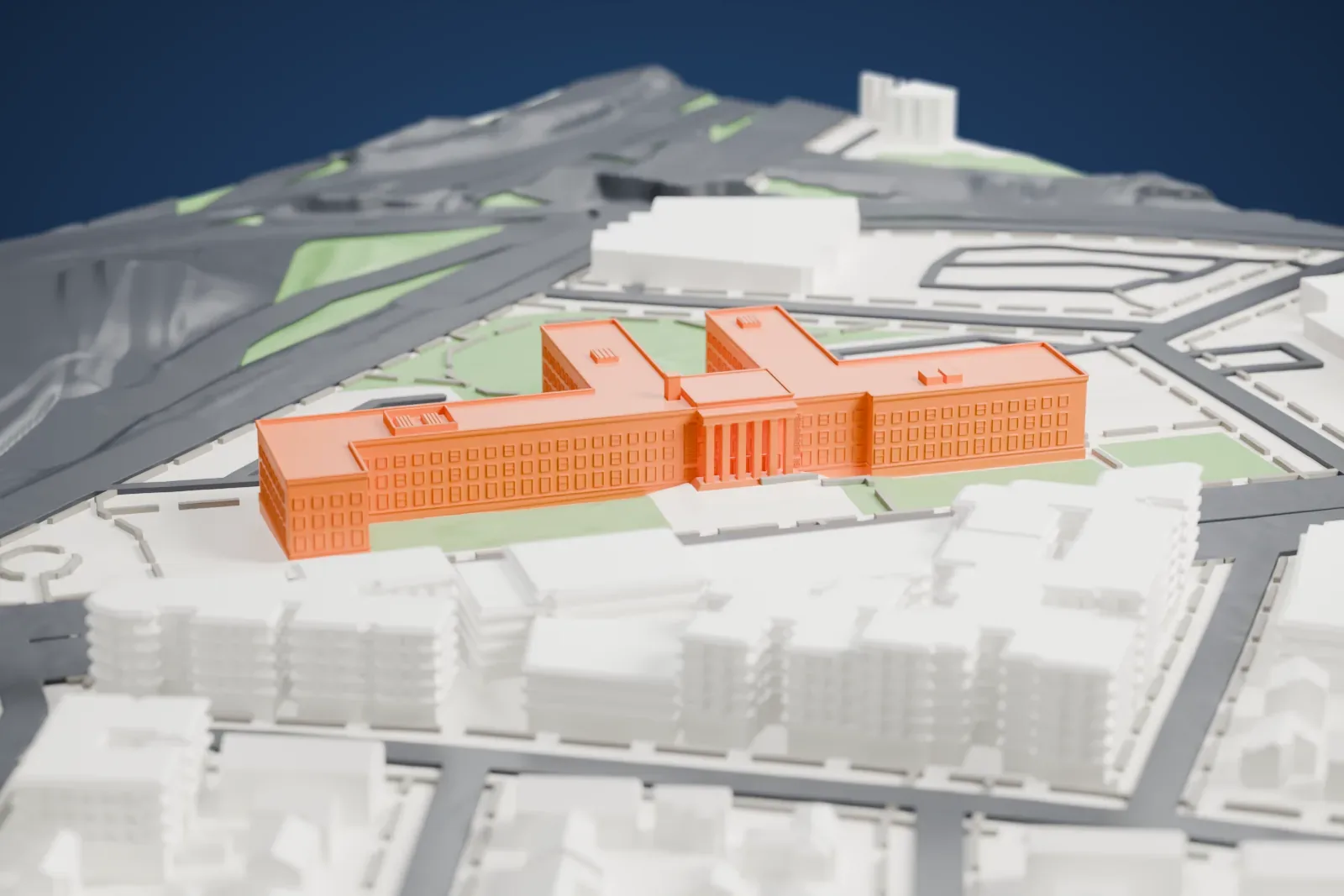 A white 3D print of Queens Borough Hall, a long four-story building of joined wings, set in a plaza and park beside wide roads.