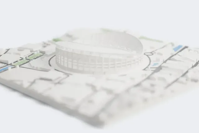 A white 3D print of Rajamangala Stadium, an oval stadium with an open braced frame and a sweeping crescent roof, surrounded by roads, large buildings and houses.