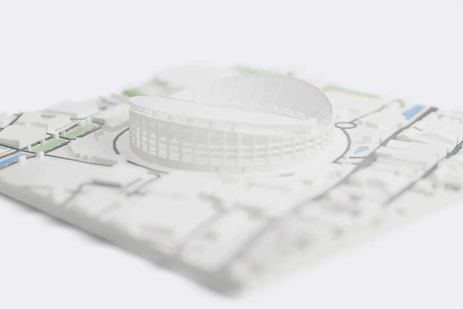 A white 3D print of Rajamangala Stadium, an oval stadium with an open braced frame and a sweeping crescent roof, surrounded by roads, large buildings and houses.