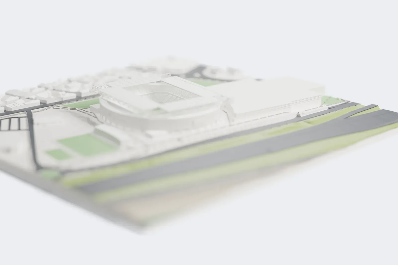 A white 3D print of RCDE Stadium, a round football stadium with a grid-like roof and corner trusses, standing on open ground beside roads and large low buildings.