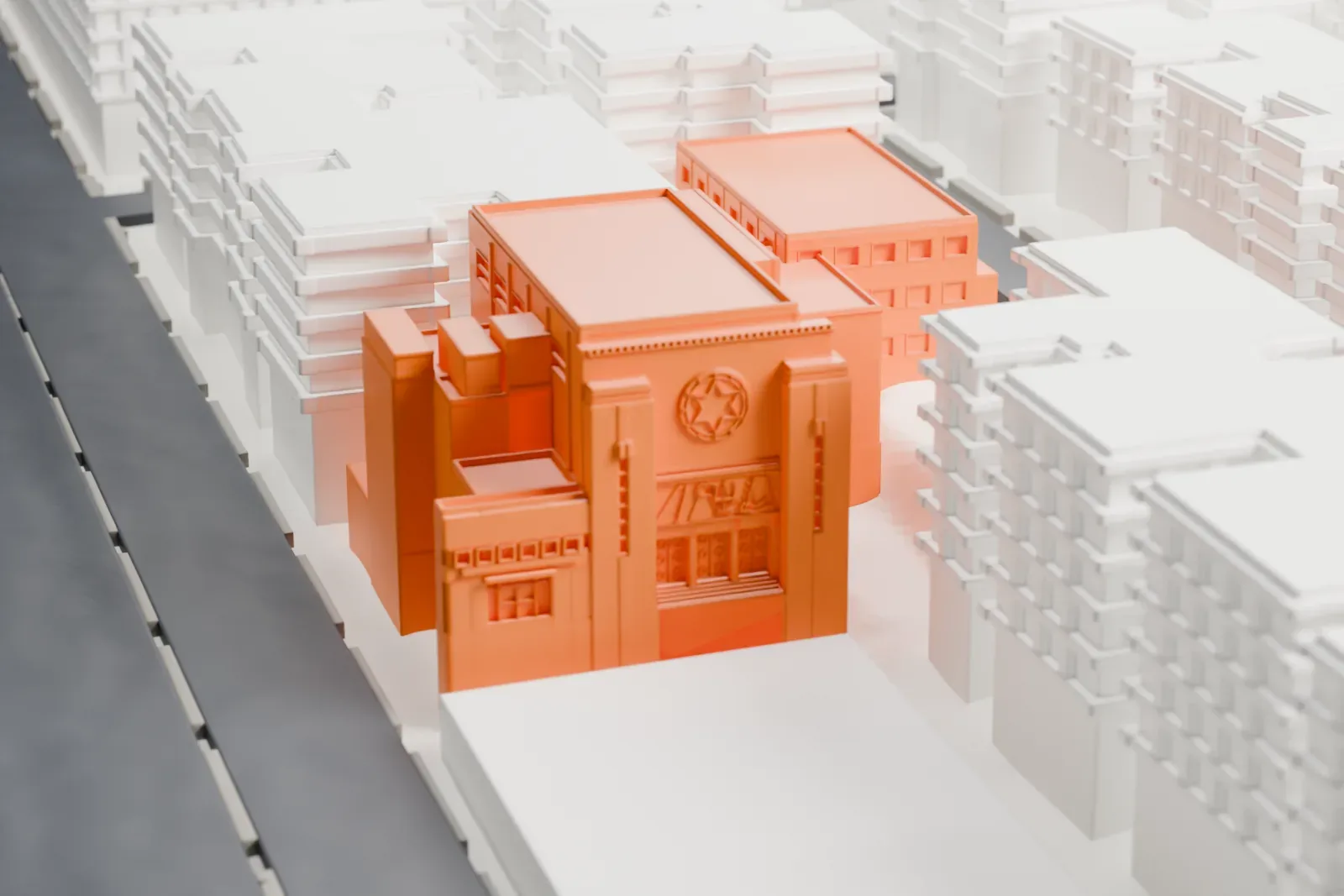 A white 3D print of the Rego Park Jewish Center, a boxy building with stepped vertical blocks and a round star emblem on its front, among lower buildings.