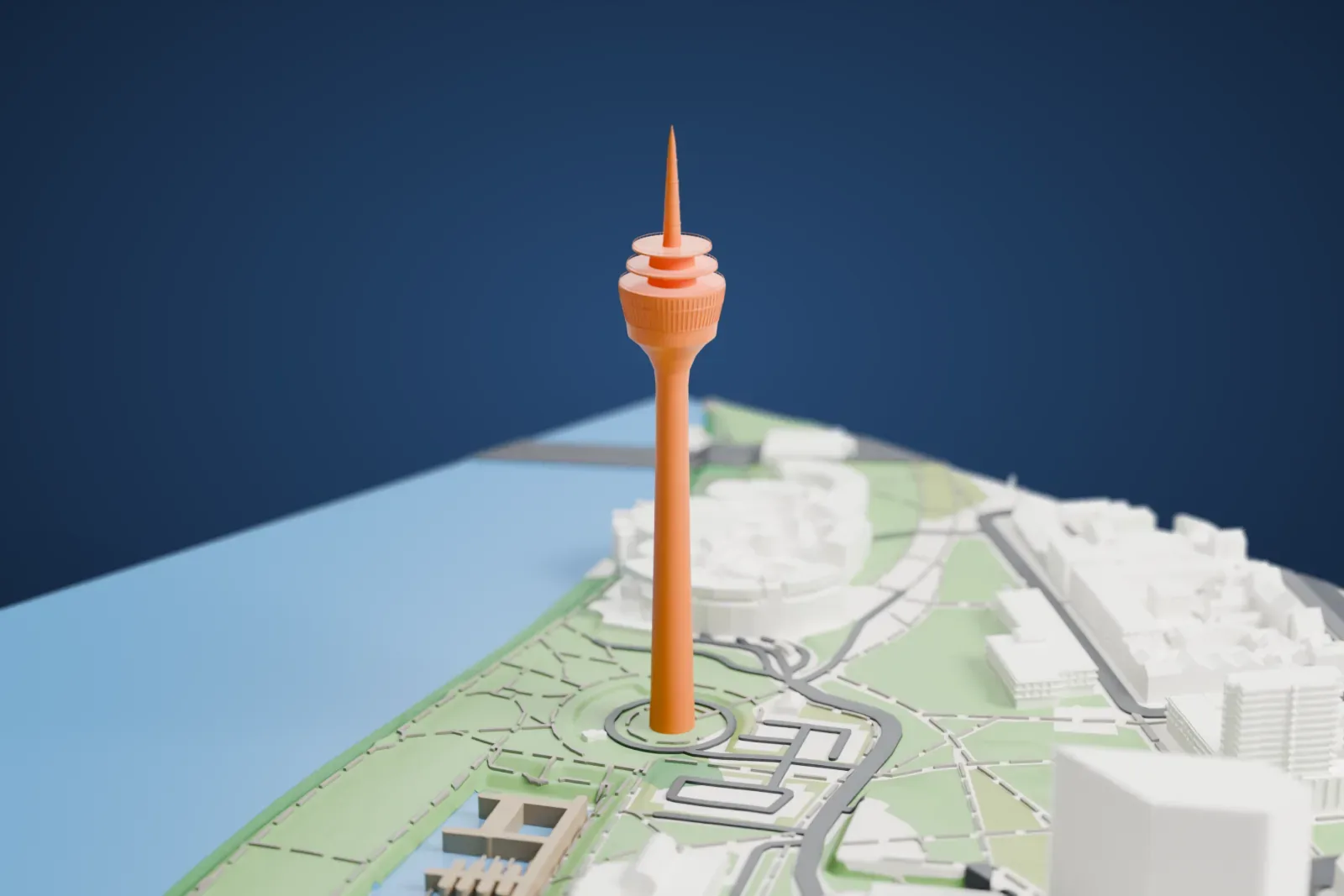 A white 3D print of the Rheinturm, a slender concrete tower with a ringed head and a thin mast, standing on green grounds beside water, with low buildings around it.