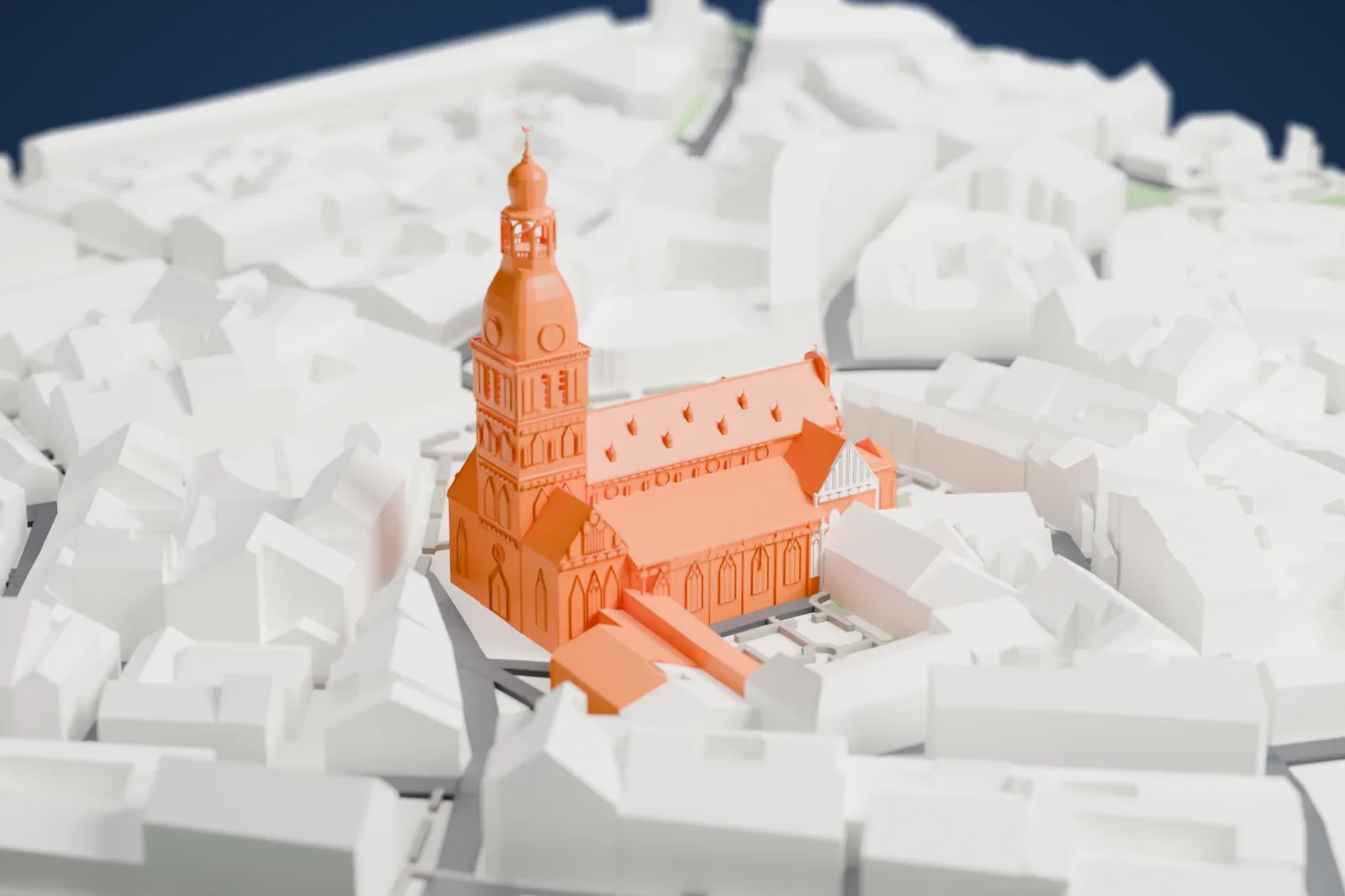 A white 3D print of Riga Cathedral, a long church with a tall tower under a rounded cap and a steep roof, surrounded by closely packed buildings and small squares.