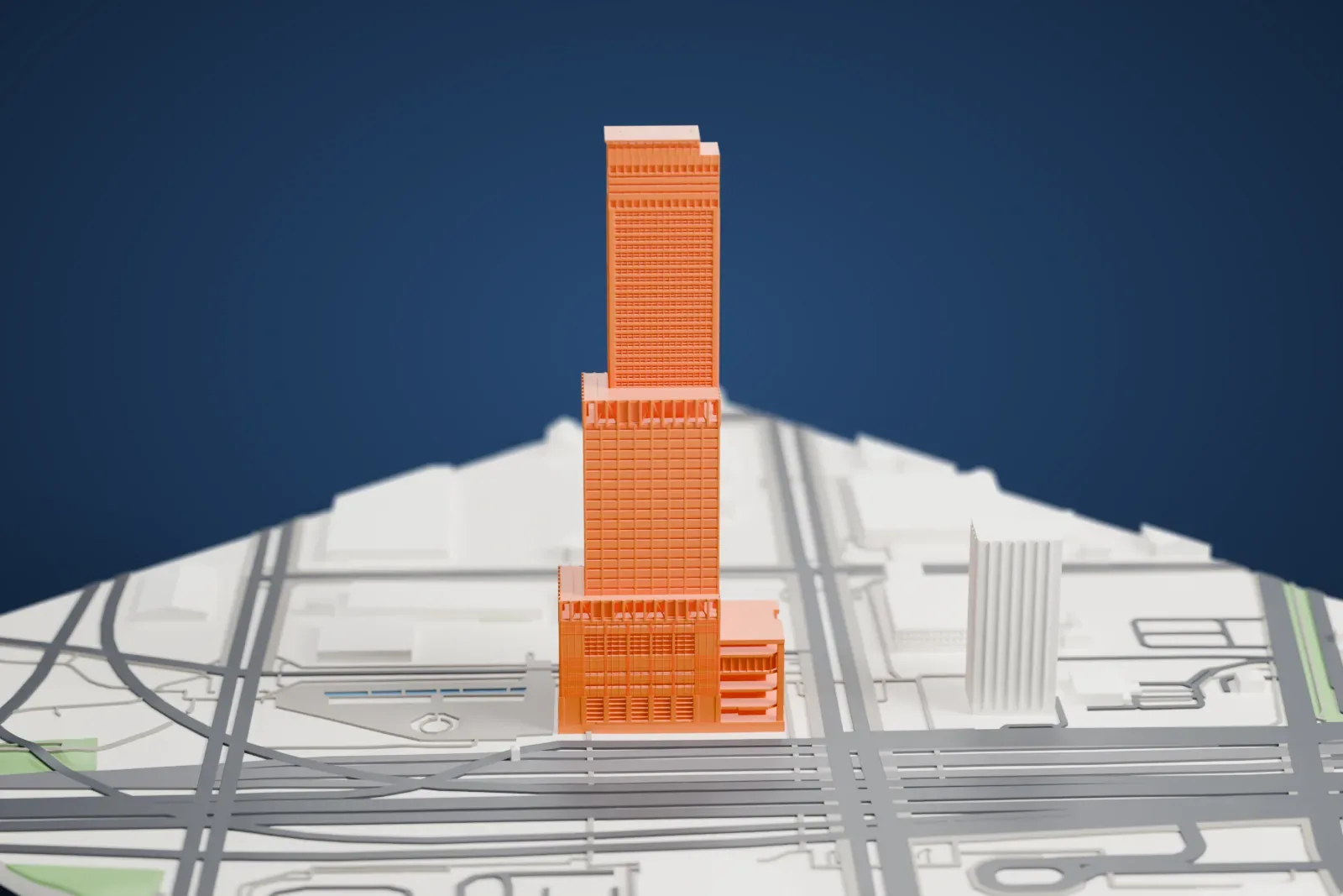 A white 3D print of the Rinku Gate Tower Building, a tall tower that narrows in three stepped sections, among surrounding roads and buildings.