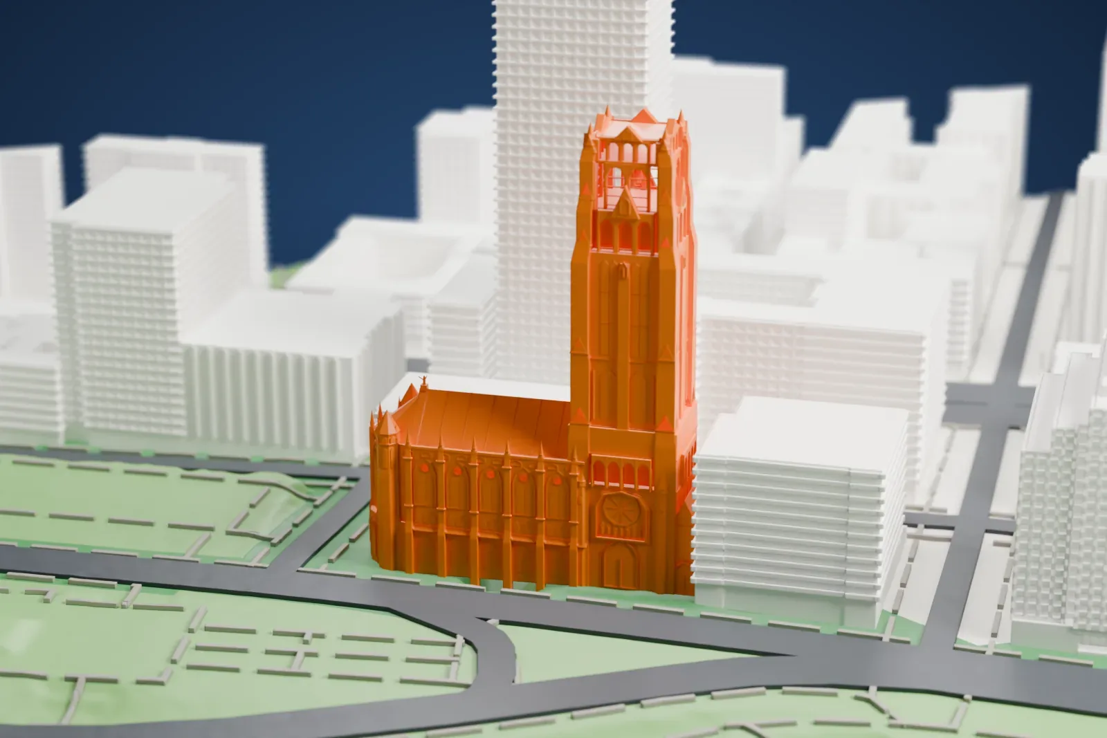 A white 3D print of Riverside Church, a Gothic-style church with a very tall square tower, beside a park and a road and among taller buildings.