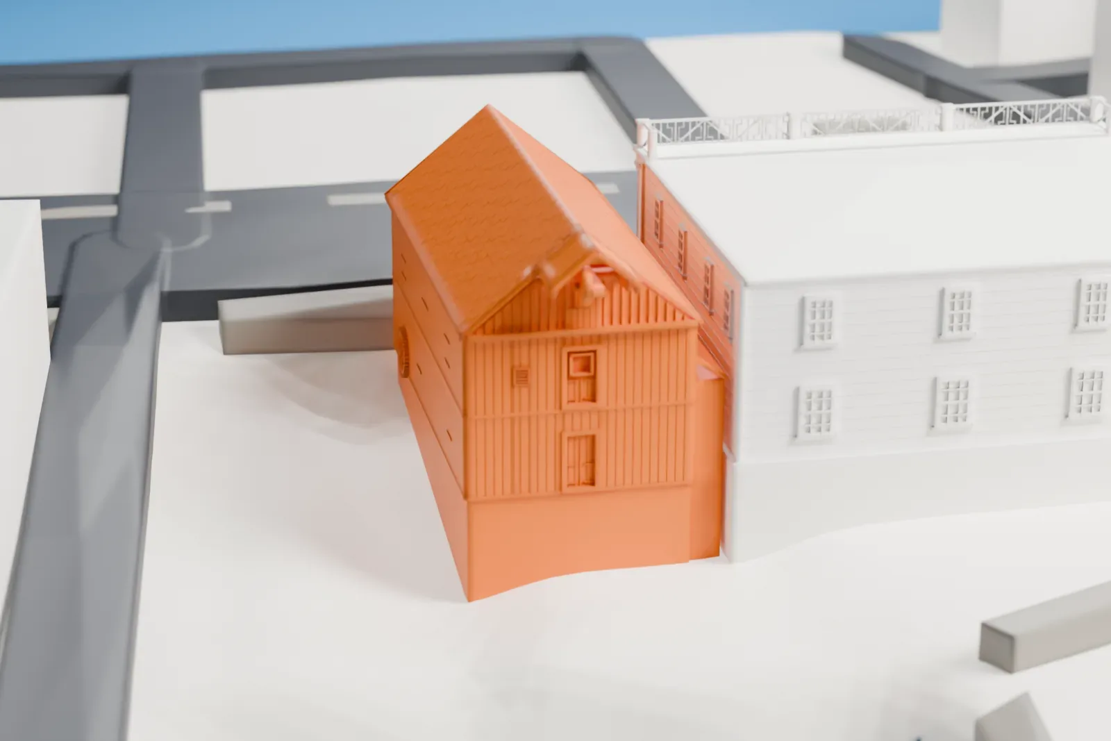 A white 3D print of the Roslyn Grist Mill, a steep-roofed timber mill beside a larger neighboring building, with a stretch of water and roads nearby.