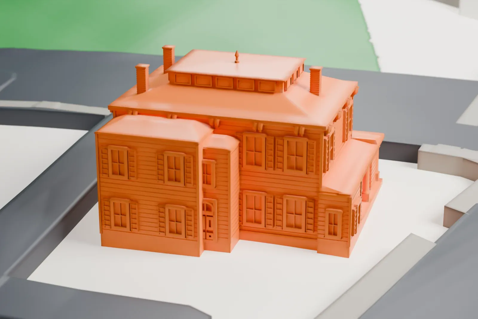A white 3D print of a two-story house with a hipped roof, a small rooftop cupola and a front porch, among roads.