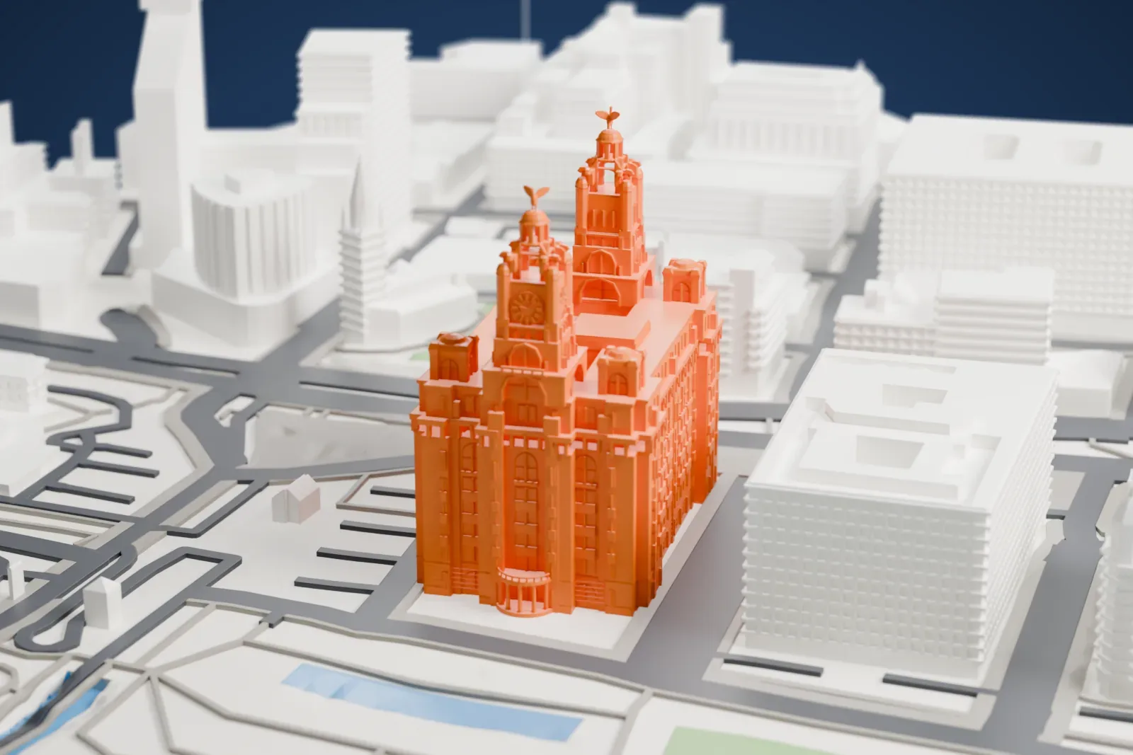 A white 3D print of the Royal Liver Building with its twin clock towers and copper Liver birds, standing at the Pier Head with the River Mersey beside it.