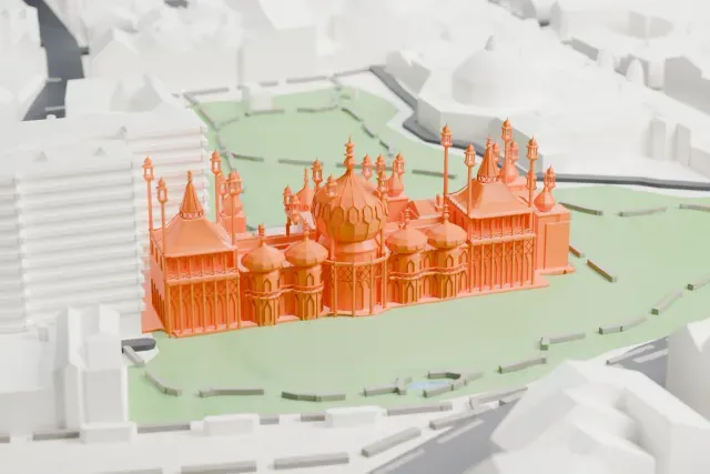A white 3D print of the Royal Pavilion, a building with a large central dome and many slender minarets, set in green gardens with streets and buildings around it.