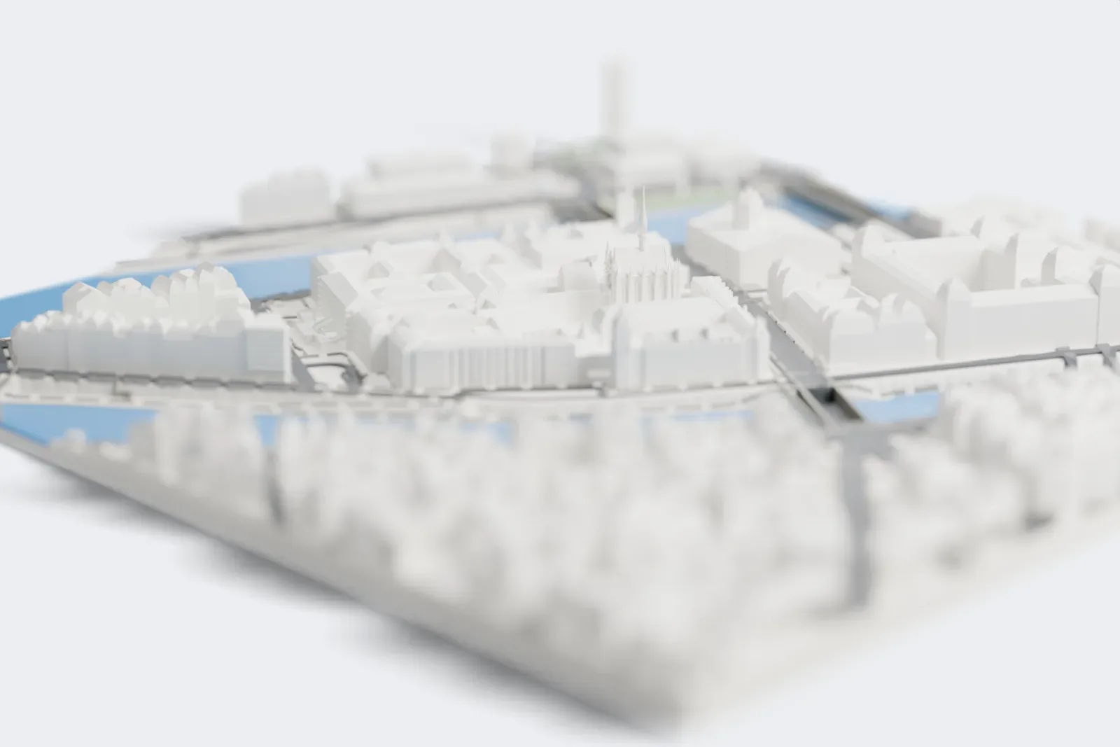 A white 3D print of the Sainte-Chapelle, a Gothic chapel with a tall slender spire and pinnacles, among large buildings with the river behind it.