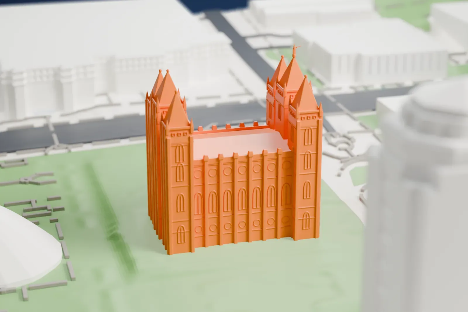 A white 3D print of the Salt Lake Temple, a building with six pointed spires and rows of arched windows, standing on a green lawn among streets and larger buildings.