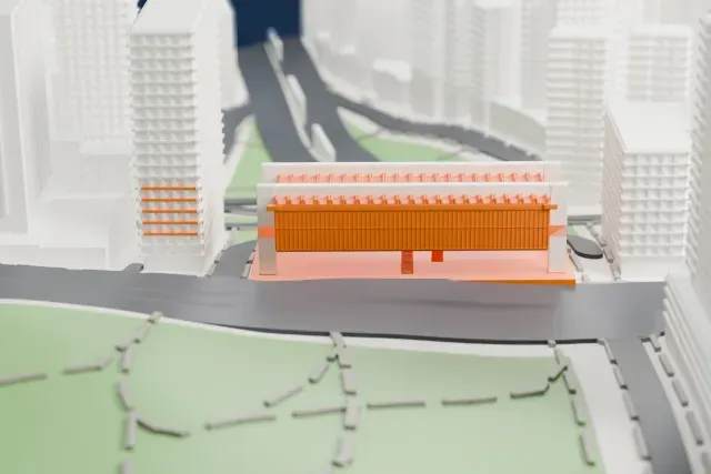 A white 3D print of the São Paulo Museum of Art, a long raised box with a ribbed roof and a broad podium, surrounded by tall buildings, roads and a park.