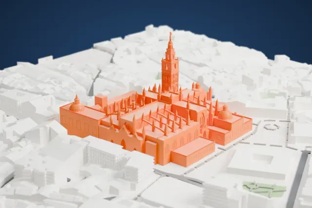 A white 3D print of Seville Cathedral, a long Gothic church with many slender pinnacles and a tall bell tower at one corner, beside an open courtyard and surrounded by dense city blocks.