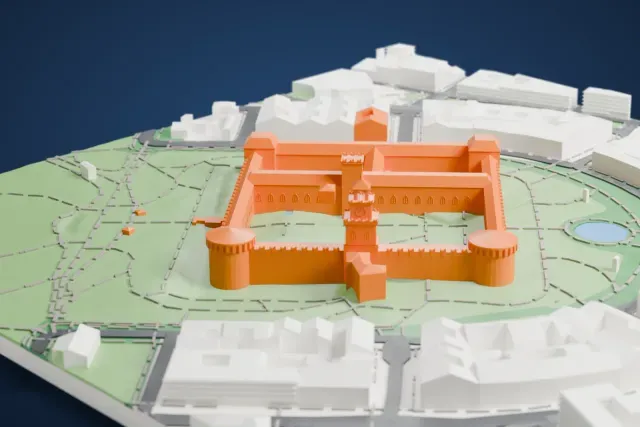 A white 3D print of Sforza Castle, a square ring of walls with round corner towers and a tall gate tower, set in a wide green park with paths and ponds and buildings around its edge.