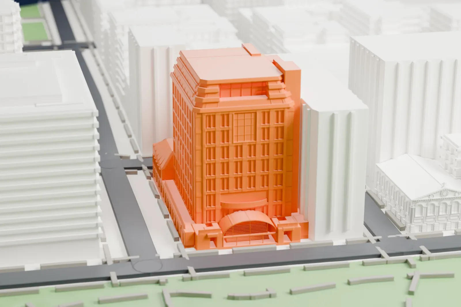 A white 3D print of the NYU Skirball building, a tall block with a stepped top and an arched entrance at its base, beside a green park and streets.